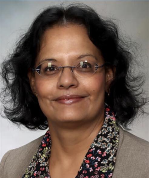 Portrait of a researcher with black, curly hair and glasses, wearing a floral blouse and blazer.